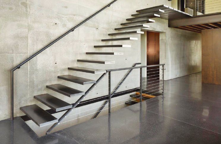 Escalera flotante de metal con baranda del mismo material. El contraste de la opacidad del cemento y el brillo del metal logran un equilibrio perfecto.
