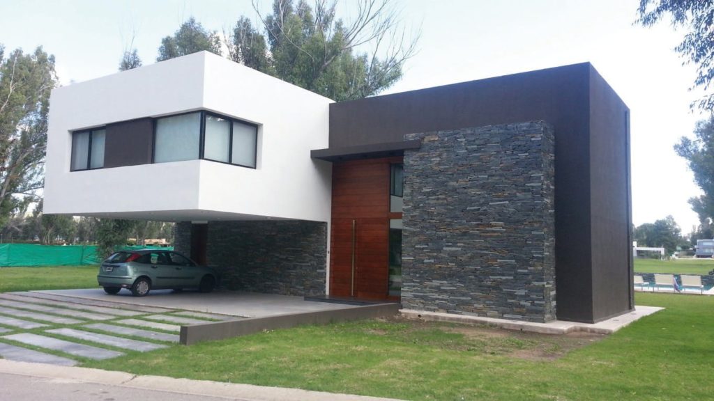 Fachada con importante movimiento al que se le añade una cálida combinación de materiales como piedra y maderas.